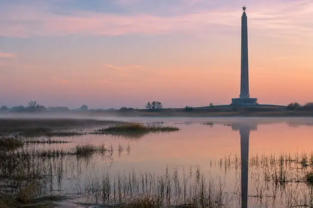 San Jacinto Monument in silhouette over misty marsh water at dawn
